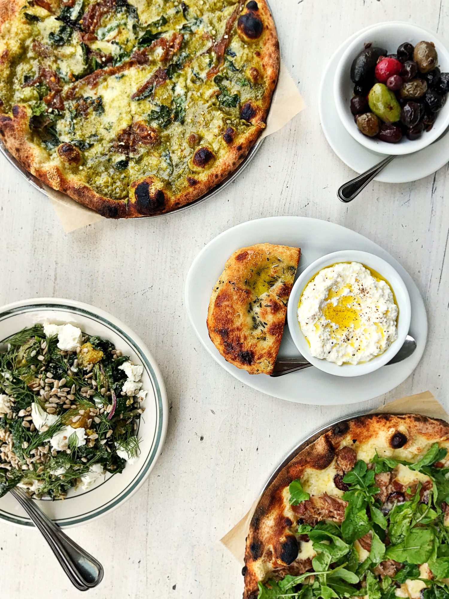Kale and pork pizzas, kale salad, olives, ricotta overhead